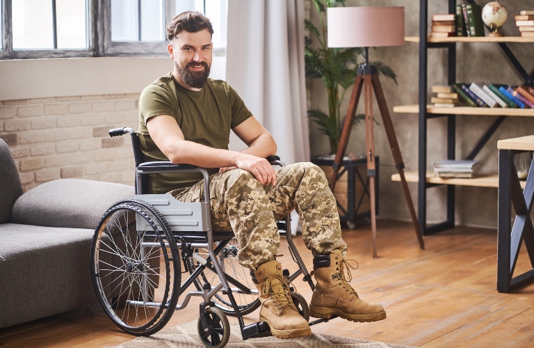 Happy young bearded veteran sitting in a wheelchair at his home